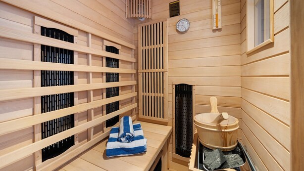 Una sala de sauna con paredes de madera, un banco, un calentador de sauna y una toalla.