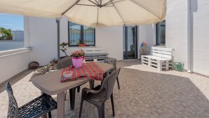 Una terrazza esterna con tavolo, sedie, un ombrellone grande e una panca.