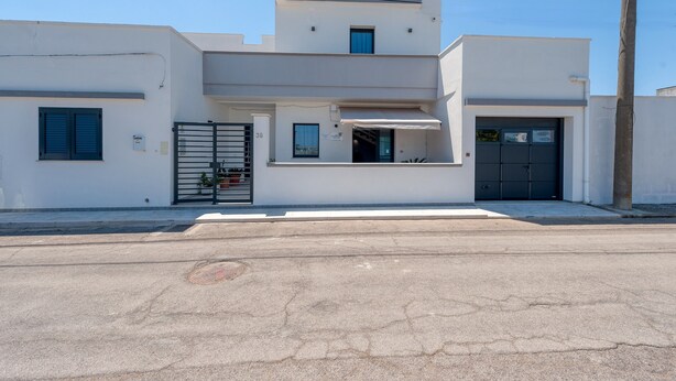 Un edificio moderno a due piani con tetto piatto, ingresso chiuso da cancello e il numero '38' ben visibile sulla parete.