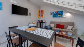 Un soggiorno moderno con tavolo da pranzo, divano e televisore a schermo piatto montato a parete.