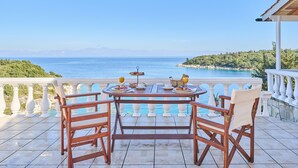 A terrace with a table set for breakfast overlooking a coastal view.