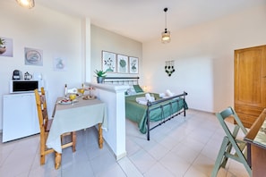 Un espacio habitable compacto con kitchenette, zona de comedor, cama con colcha verde y armario de madera.