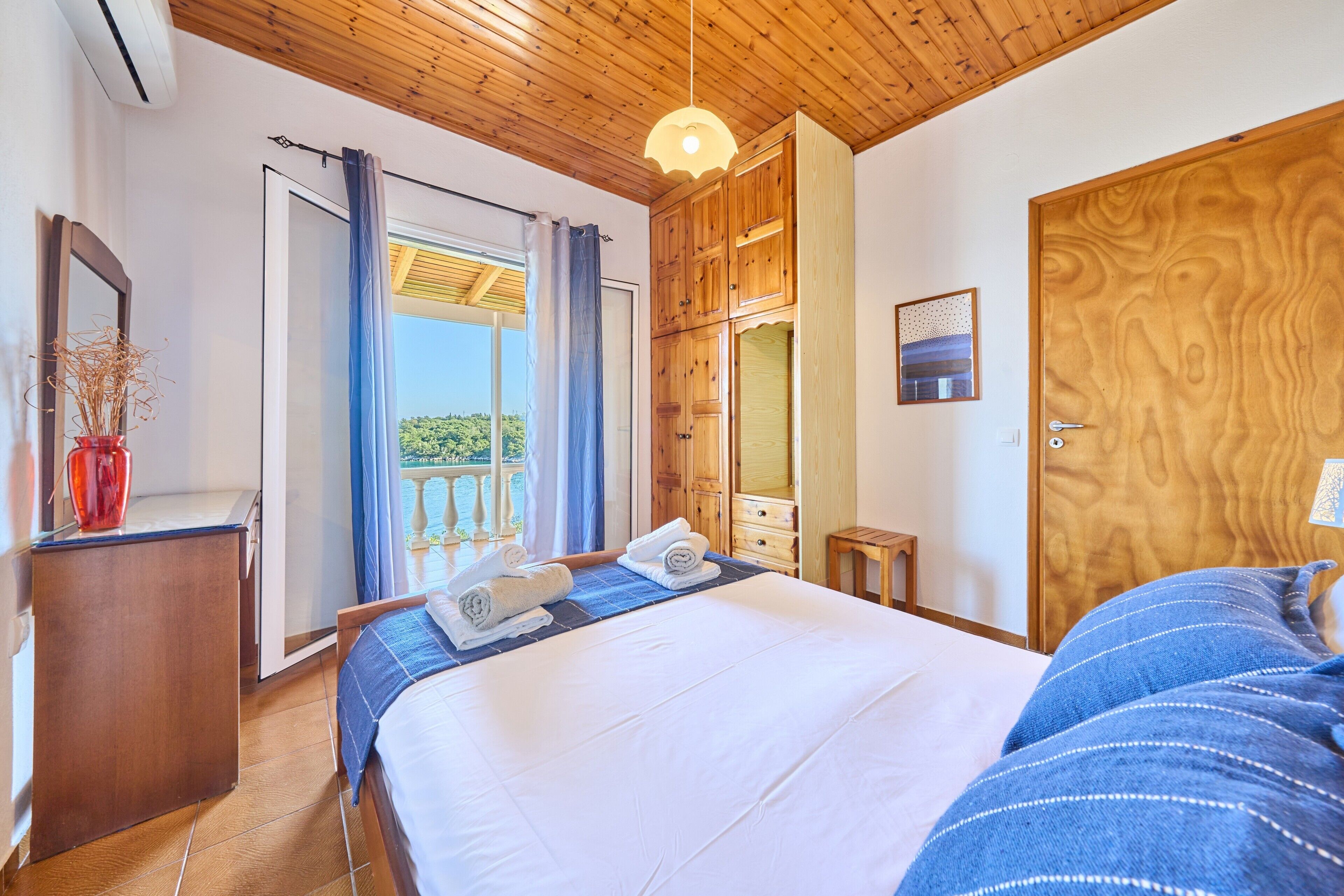 Un dormitorio con cama, armario de madera, una mesita y una ventana con cortinas.