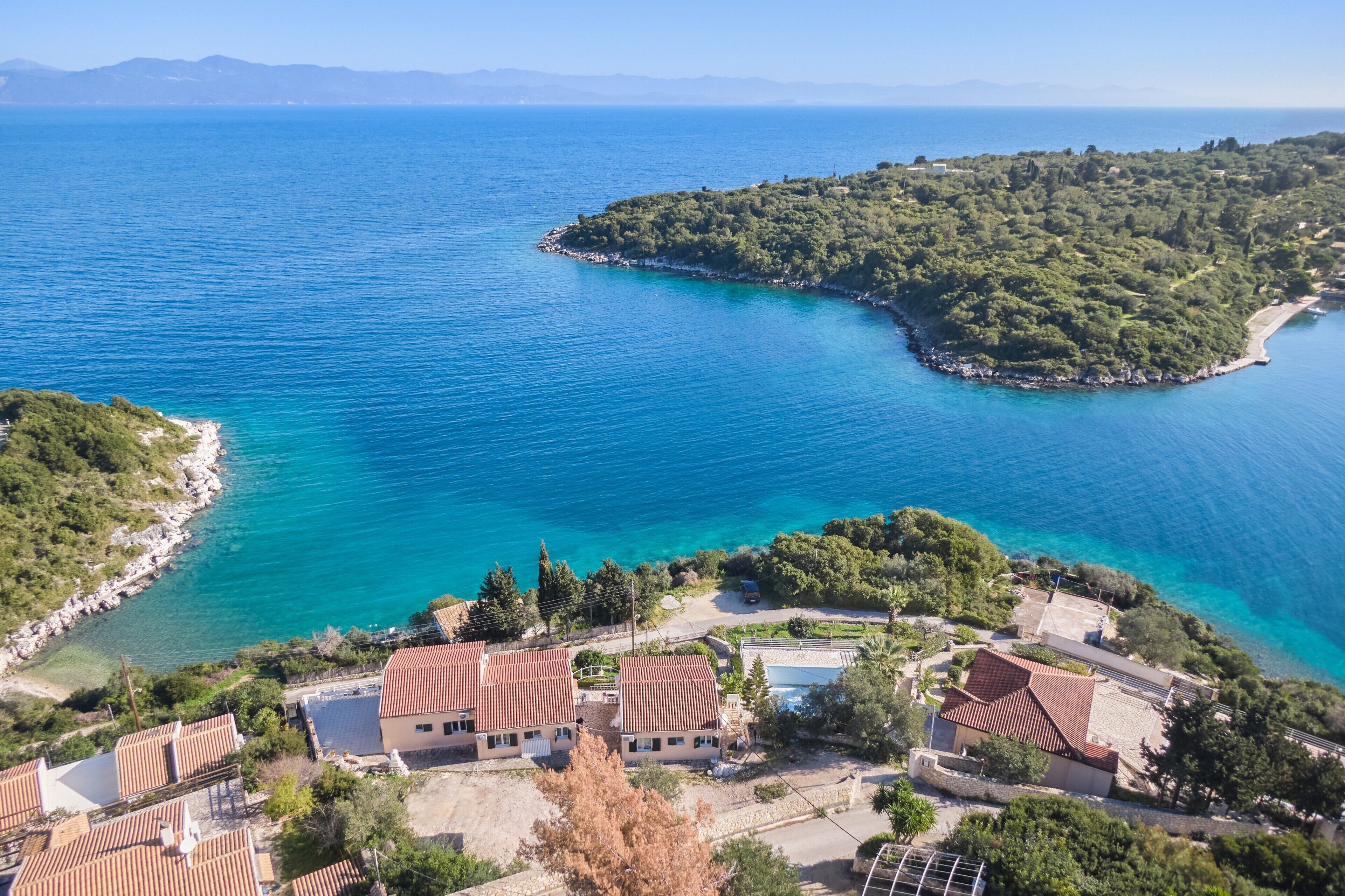 Un village côtier avec des maisons à étages, une mer d’un bleu limpide et une petite île à la végétation luxuriante.