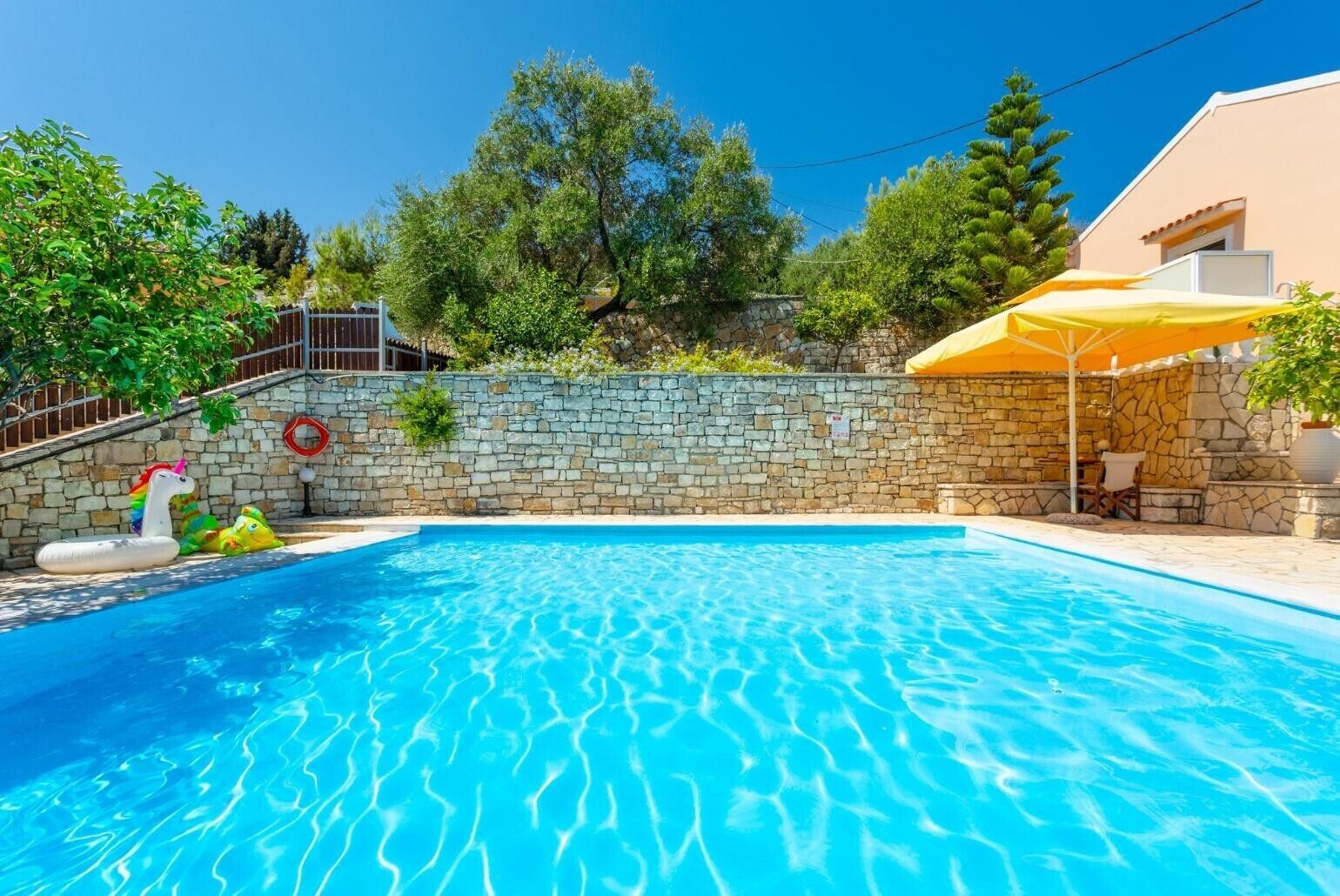 Une piscine avec des murs en pierre, un escalier en pierre et un parasol jaune.