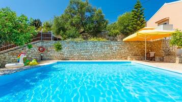Une piscine avec des murs en pierre, un escalier en pierre et un parasol jaune.