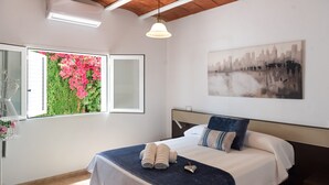 A bedroom with a bed, a window with a view of pink flowers, a cityscape painting, and a birdcage with flowers. - Holiday Home 'Susana' with Private Pool, Private Terrace and Wi-Fi (Santa Eulària des Riu)