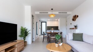 A modern living room with a flat-screen TV, a dining area with a wooden table and chairs, a sofa, and a kitchen in the background. - Apartment 'Middle Views West' with Sea View, Wi-Fi and Air Conditioning (Fuengirola)