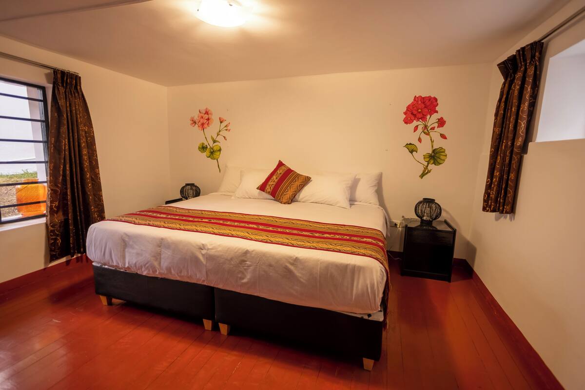 Une chambre à coucher avec un grand lit, une table de chevet et une fenêtre avec des rideaux.