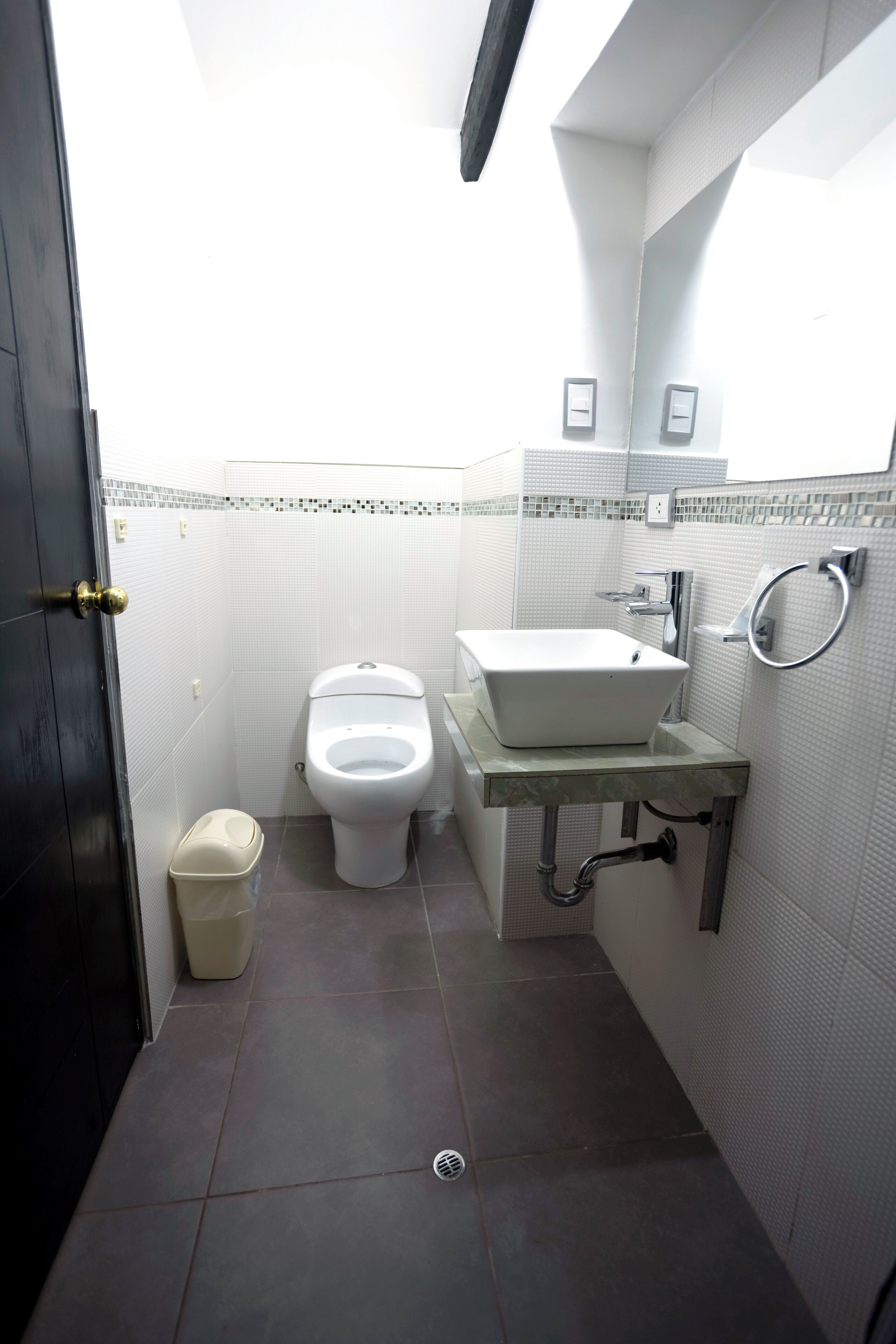 A compact bathroom with a toilet, sink, and trash bin.