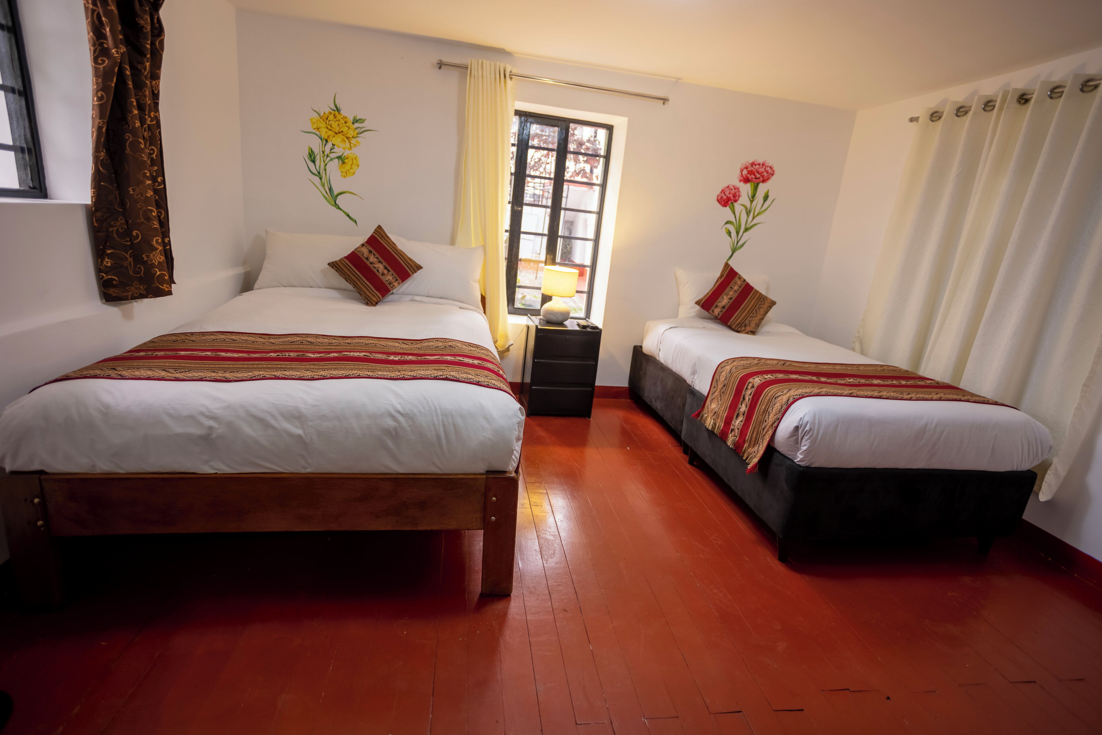 Habitación de hotel con dos camas, una mesita de noche, una ventana con cortinas y suelo de madera.