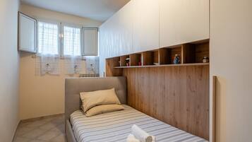 A bedroom with a bed, a headboard, a window with curtains, and a wooden shelf with items.