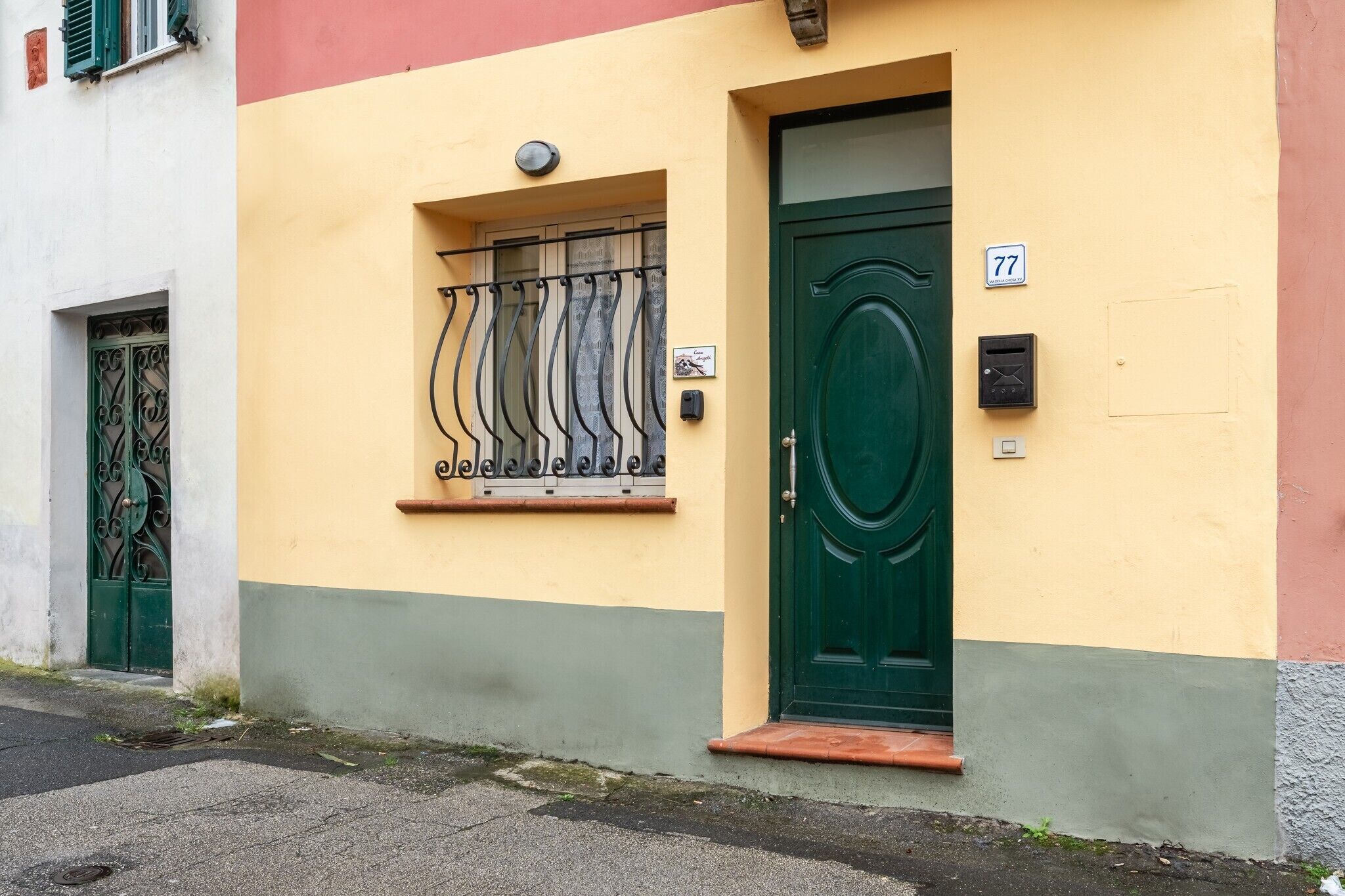 A building with a green door, a window with metal bars, and a number '77' on the wall.