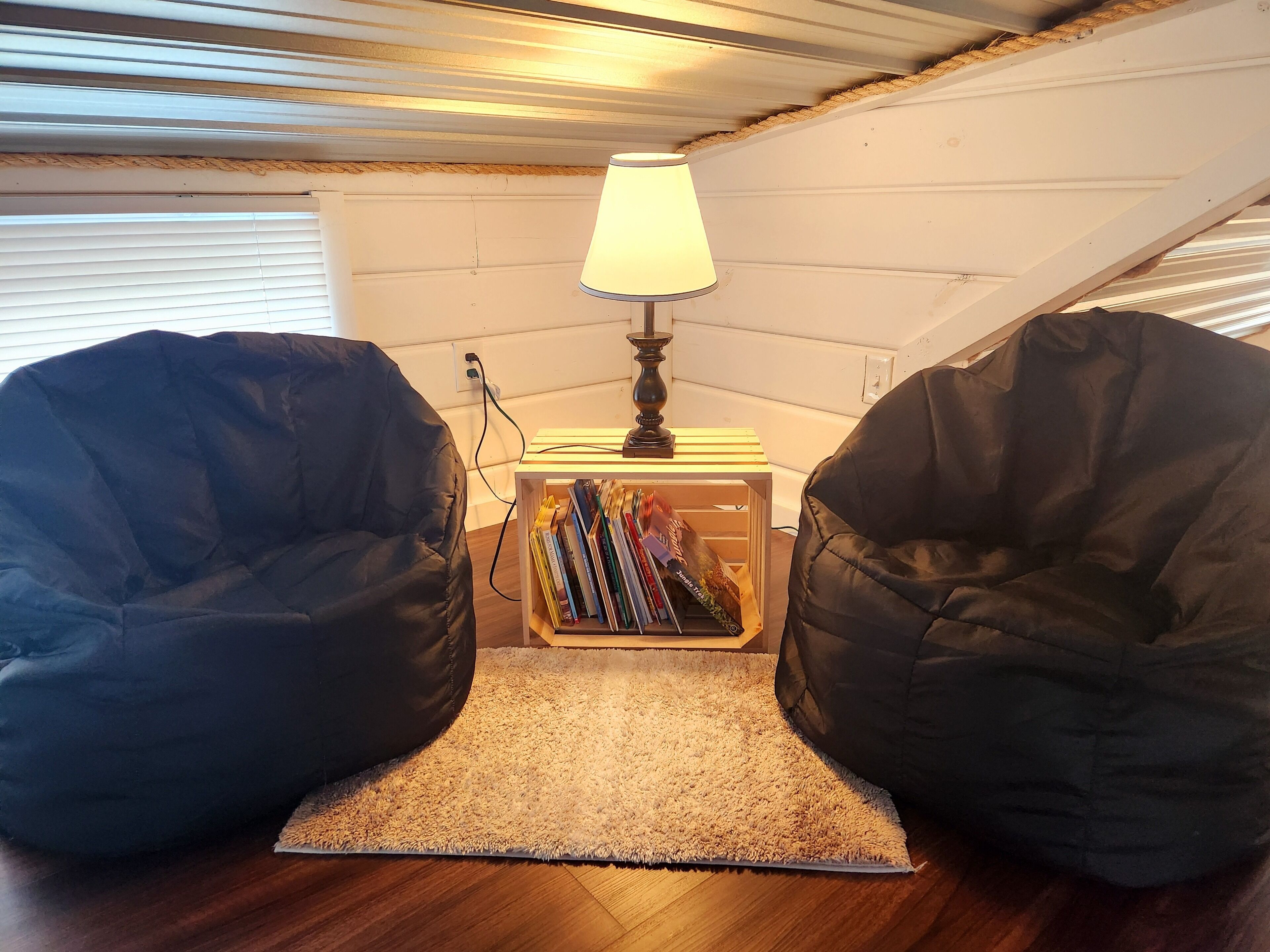 Ein gemütlicher Lesebereich mit zwei Sitzsäcken, einem kleinen Tisch mit Lampe und einem Bücherregal.