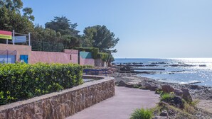 A coastal walkway with a stone wall, a bench, and a building with a sign. - Apartment 'St Raphael' with Balcony and Wi-Fi (Saint-Raphaël)