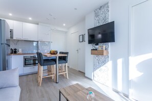 A modern kitchen with white cabinets, a built-in oven, and a dining area with a table and chairs.