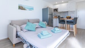 A modern room with a bed, a sofa, a dining table with chairs, a kitchen area, and a small window. - Apartment 'St Raphael' with Balcony and Wi-Fi (Saint-Raphaël)