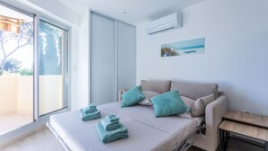 A modern bedroom with a bed, pillows, a bedside table, and an air conditioning unit. - Apartment 'St Raphael' with Balcony and Wi-Fi (Saint-Raphaël)