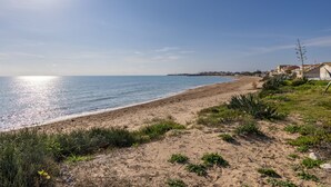 Una playa con cielo despejado, orilla arenosa y edificios al fondo.