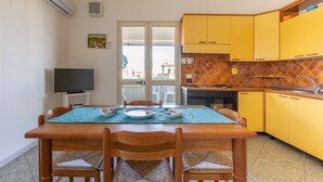 Un comedor con una mesa dispuesta para cuatro personas, un televisor y una cocina con armarios amarillos.