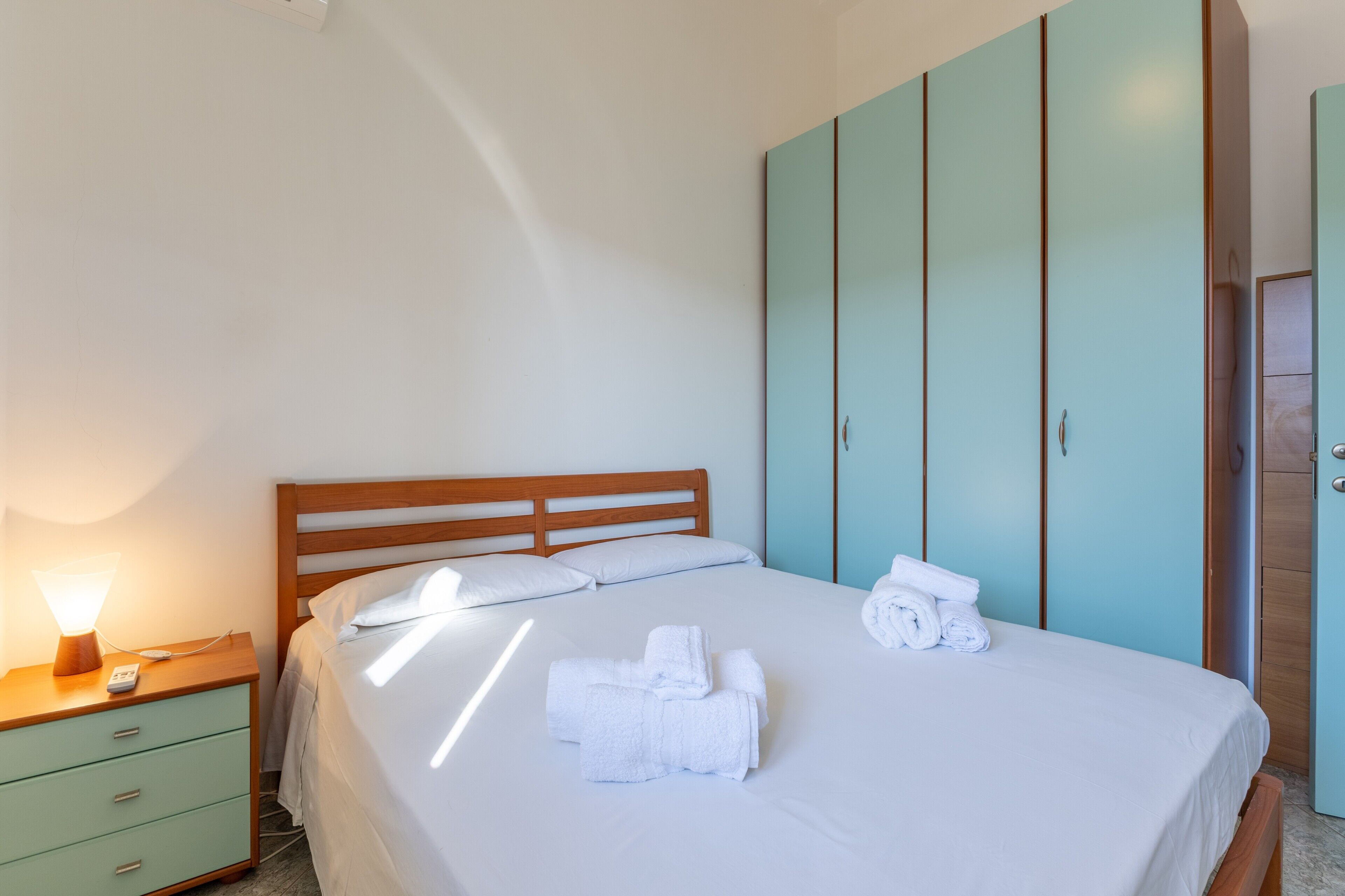 A neatly made bed with white linens, a wooden headboard, and a nightstand with a lamp.