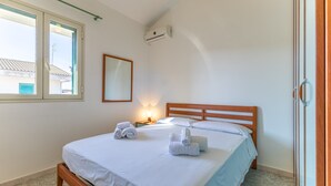 Un dormitorio con una cama de madera, ropa de cama blanca, una lámpara de noche y una ventana con persianas.