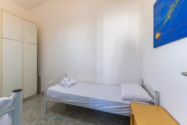 A single-bed room with a white bed, a wooden nightstand, a wardrobe, and a painting on the wall.