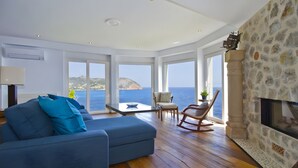 A room with a blue sofa, a wooden floor, a stone fireplace, and large windows overlooking the sea. - Villa 'Blanca' with Sea View, Wi-Fi and Air Conditioning (Capdepera)