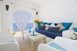 A room with a view of the sea, a white sofa with blue cushions, a white table with a vase of flowers, and a white chair. - Villa 'Blanca' with Sea View, Wi-Fi and Air Conditioning (Capdepera)