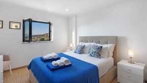 Une chambre à coucher avec un lit, une table de chevet, une fenêtre donnant sur un beau paysage et une chaise.