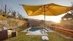 Une piscine avec un parasol jaune, un mur en pierre et du mobilier d’extérieur.