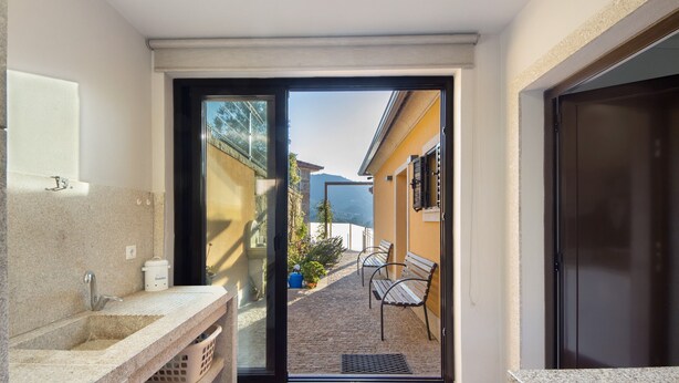 Une salle de bain équipée d’un lavabo, d’un miroir et d’une porte donnant sur un balcon avec vue sur les bâtiments et les montagnes.