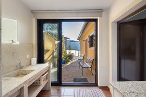A bathroom with a sink, a mirror, and a door leading to a balcony with a view of buildings and mountains.