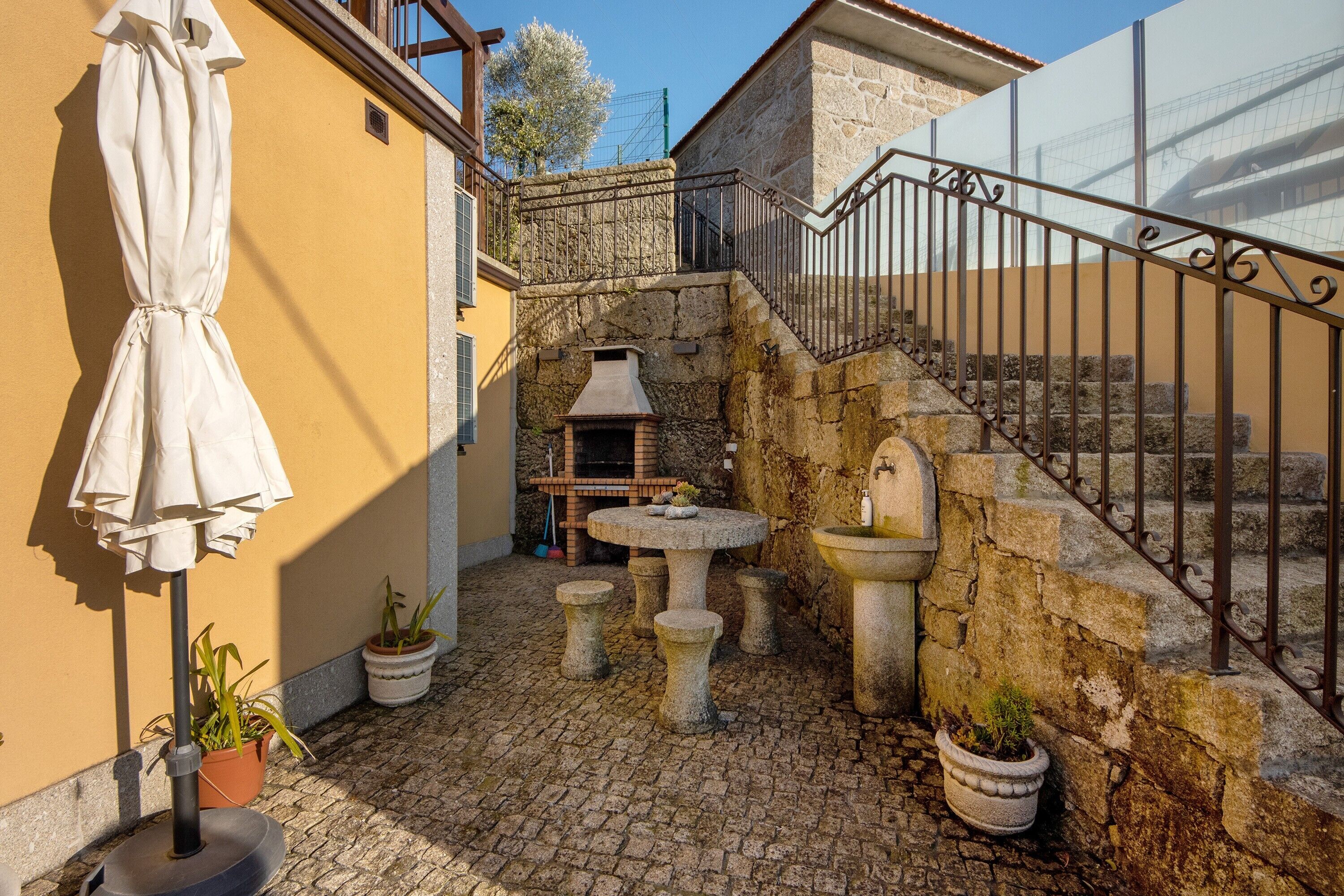 Une cour avec des marches en pierre, une table en pierre, des plantes en pot et un barbecue.