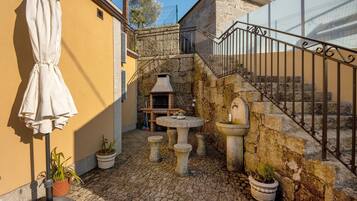 Une cour avec des marches en pierre, une table en pierre, des plantes en pot et un barbecue.