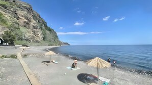 Una playa con un acantilado rocoso, un camino pavimentado y algunas sombrillas.