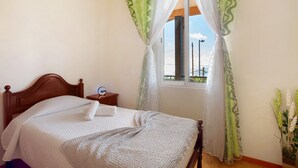 Un dormitorio con cama de madera, una mesita de noche, una ventana con cortinas y vista al cielo.