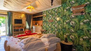 Une chambre avec un lit, une télévision, une cheminée et un papier peint aux motifs tropicaux.