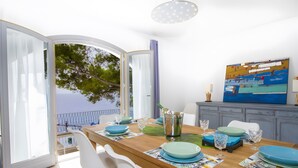 An open dining area with a view of the sea, a dining table set with plates and glasses, and a painting on the wall. - Holiday Home 'Blanca' with Sea View, Wi-Fi and Air Conditioning (Provensals)