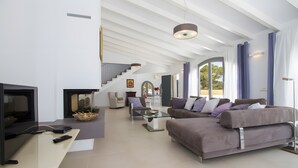 A modern living room with a flat-screen TV, sofa, and a staircase leading to another level. - Holiday Home 'Blanca' with Sea View, Wi-Fi and Air Conditioning (Provensals)