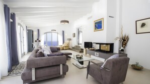 A modern living room with a sofa, armchair, TV, and a fireplace. - Holiday Home 'Blanca' with Sea View, Wi-Fi and Air Conditioning (Provensals)