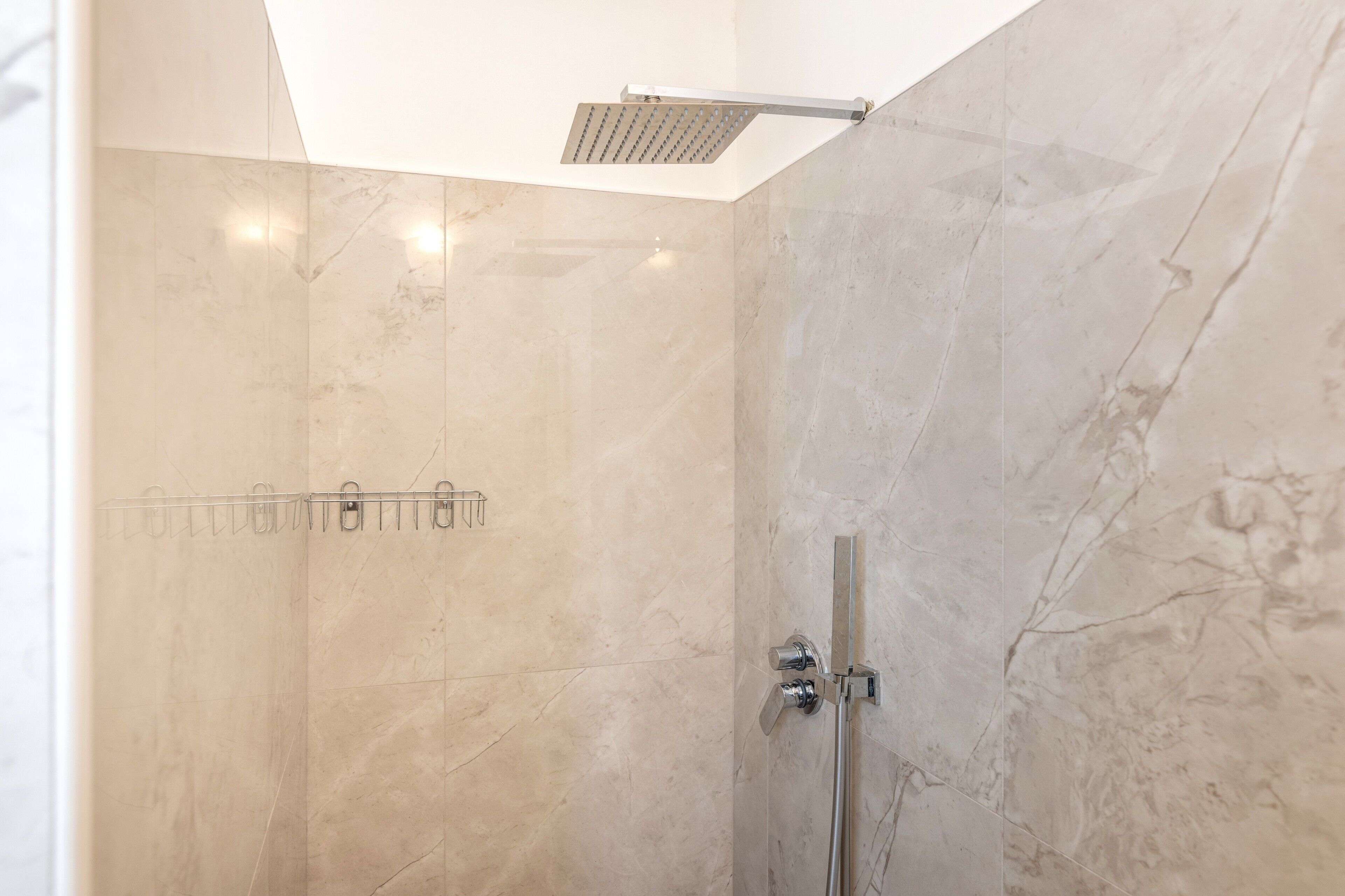A modern shower with a glass door, a handheld showerhead, and a wall-mounted control panel.