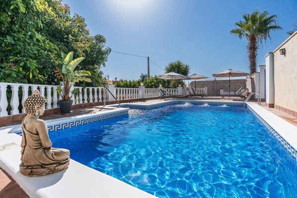 A swimming pool with a Buddha statue, surrounded by a white fence, palm trees, and umbrellas.