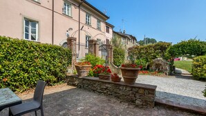 A building with a stone wall, potted plants, and a chair. - Apartment 'La Castellana' with Shared Pool, Wi-Fi and Air Conditioning (Massarosa)
