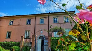 A building with a symmetrical facade, multiple windows, a central entrance with a decorative arch, and a gated entrance. - Apartment 'La Castellana' with Shared Pool, Wi-Fi and Air Conditioning (Massarosa)
