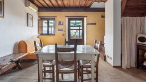 A dining area with a wooden table, chairs, and a bench. There are windows with curtains, a wooden ceiling, and a view outside. - Apartment 'La Castellana' with Shared Pool, Wi-Fi and Air Conditioning (Massarosa)