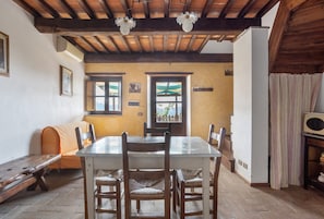 Un coin repas avec une table en bois, des chaises et un banc. On y trouve des fenêtres avec des rideaux, un plafond en bois et une vue sur l’extérieur.