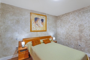 A bedroom with a bed, nightstands, a lamp, and a painting on the wall.