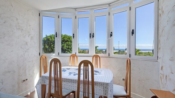 Un área de comedor con mesa y sillas, ventanas amplias y vista al mar.