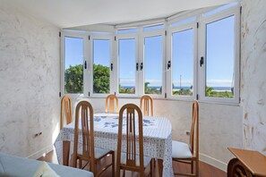 Un espace repas comprenant une table et des chaises, de grandes fenêtres et une vue sur la mer.